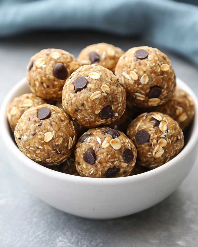 Homemade energy balls arranged on a white plate with sliced nuts, oats, and chocolate chips.